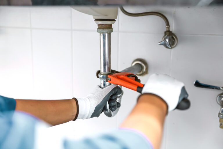 Plumber using a wrench to repair a water pipe under the sink